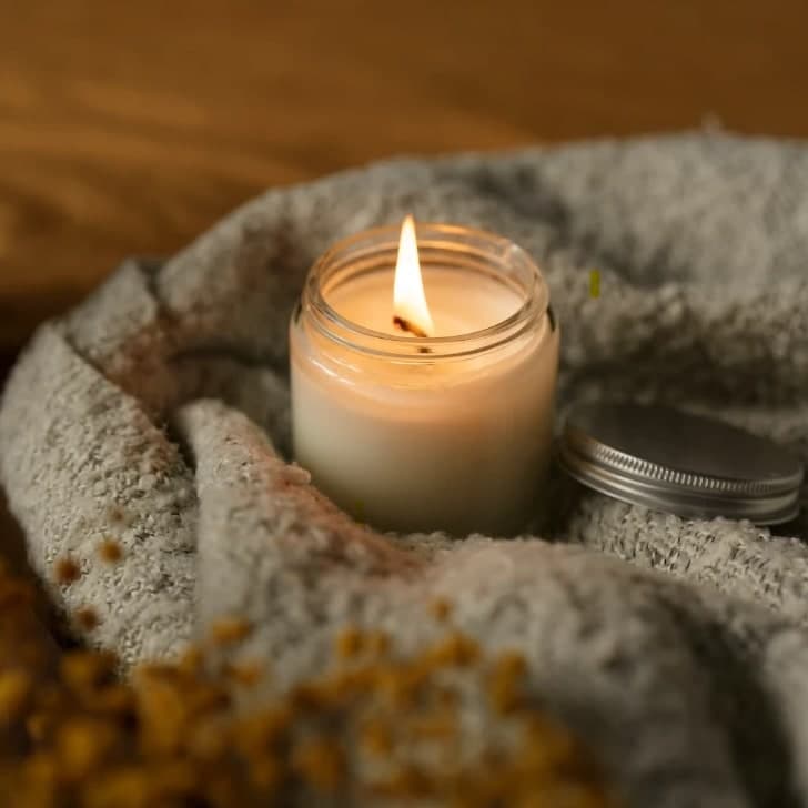 A lit candle in a glass jar nestled in a soft knitted blanket